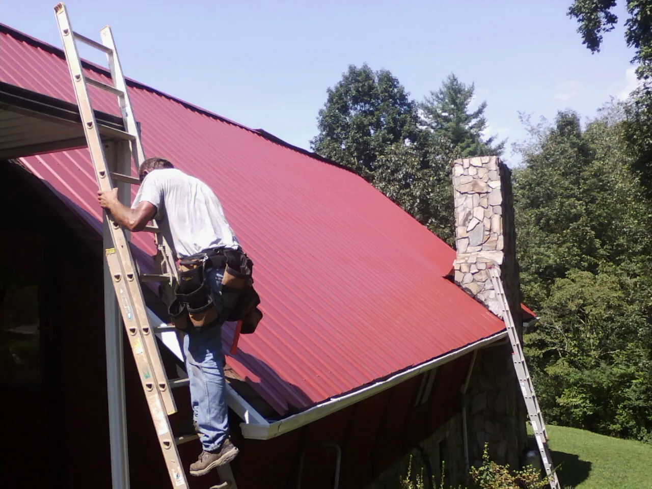 Roofer on a ladder beside a red metal roof and stone chimney in Courtland